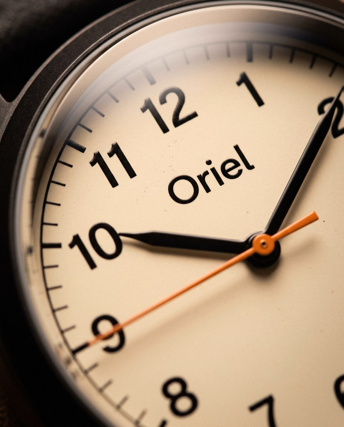 Close up of the cream dial: the Oriel name, black numerals and hands, and the orange seconds hand.