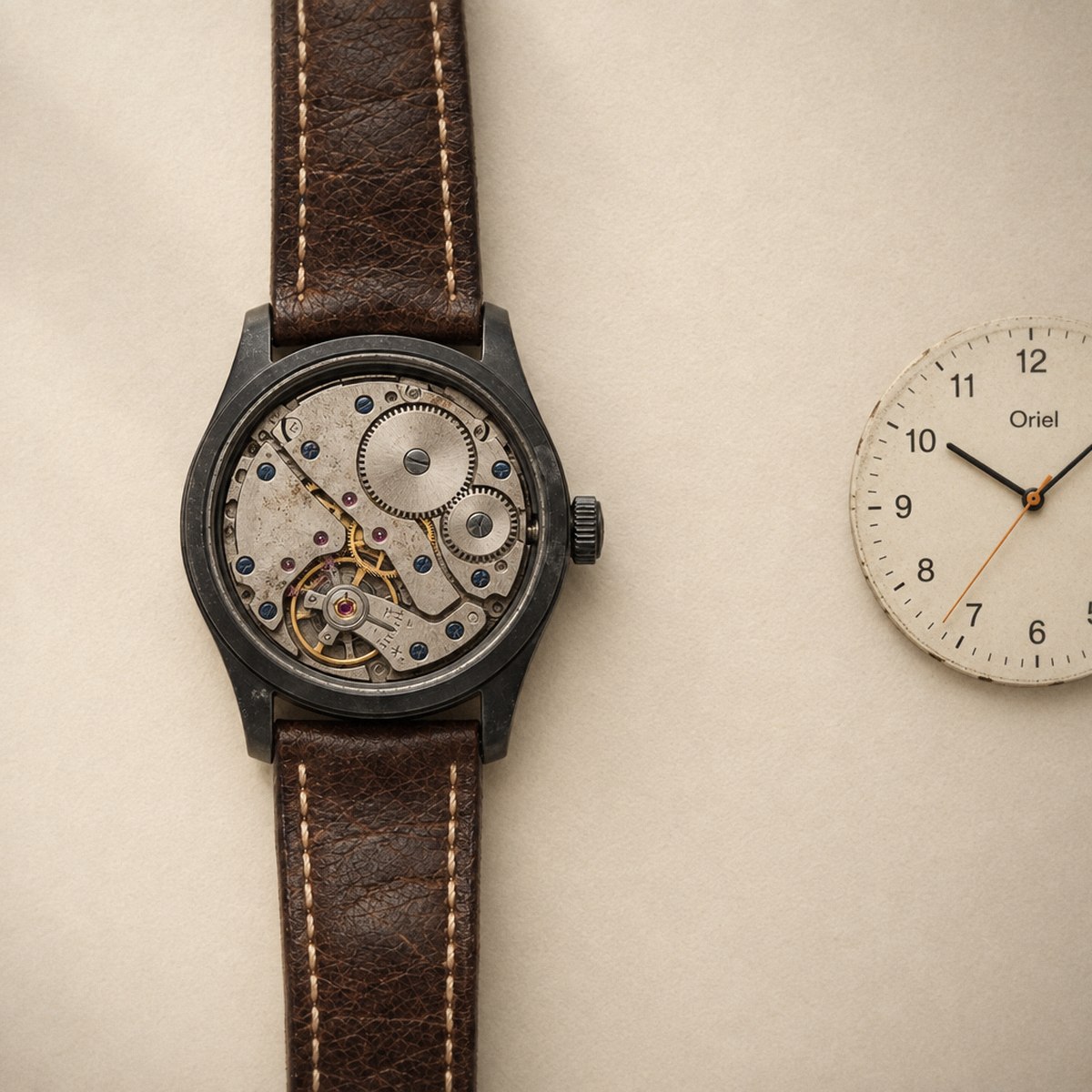 The open case from above with the dial out: the mechanical movement sits inside, the cream dial cartridge beside it on the paper.